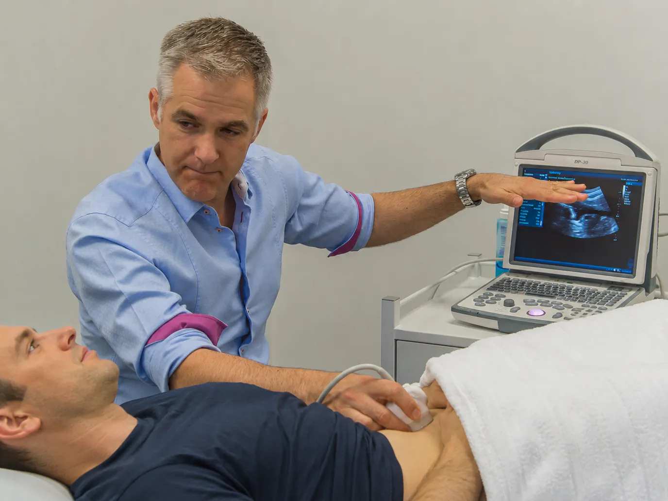 Nathan scanning a man’s lower abdomen and pointing to the muscle movement on the ultrasound screen